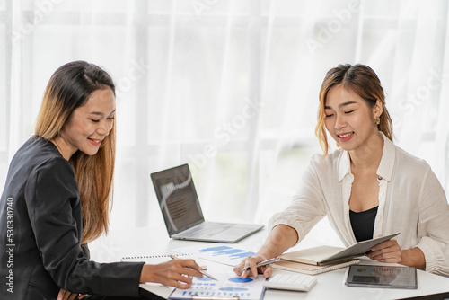 A team of Asian businesswomen discussing something and smiling as they sit at a desk in the office of women working together analyzing finances.