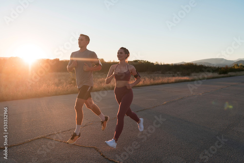 healthy young couple jogging in the city streets in the early morning with a beautiful sunrise in the background. 