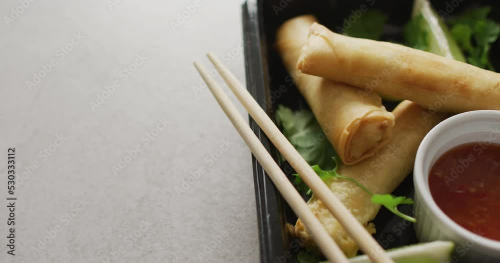 Composition of plate with spring rolls and chilli sauce with chopsticks on grey background