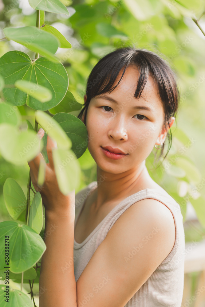 Beautiful woman face portrait with green leaf. Beauty face. Woman model with natural makeup and healthy skin in tropical nature. Beautiful asian girl portrait with jungle leaves on background. Beautiful woman face portrait with green leaf. Beauty face. Woman model with natural makeup and healthy skin in tropical nature. Beautiful asian girl portrait with jungle leaves on background.