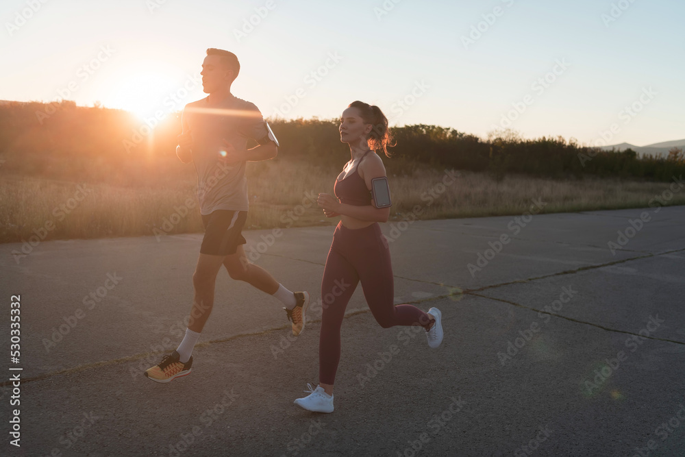Fototapeta premium healthy young couple jogging in the city streets in the early morning with a beautiful sunrise in the background.