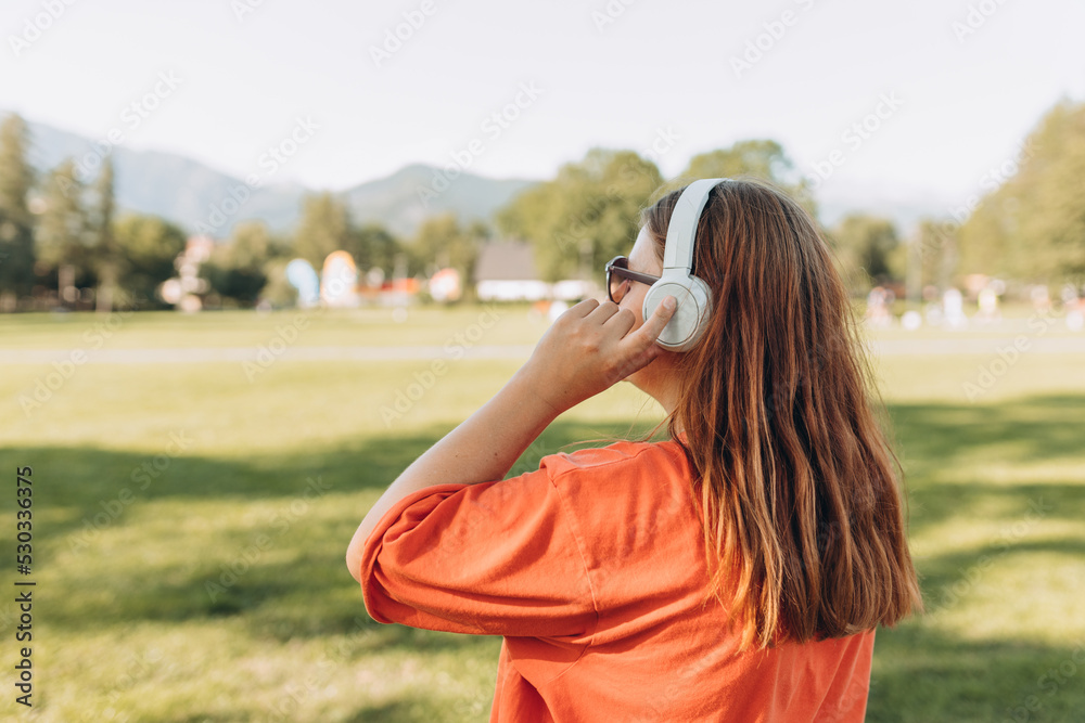 Woman in headphones listening music in nature at the mountains. Healthy and active lifestyle concept. Back view. Music lover enjoying music.