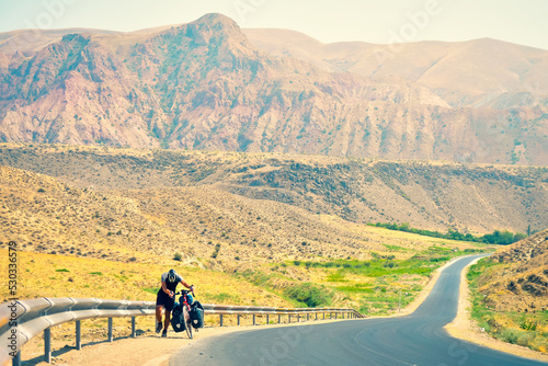 Obraz na plátně Caucasian male cyclist push his heavy touring bicycle uphill in extreme heat outdoors in mountains
