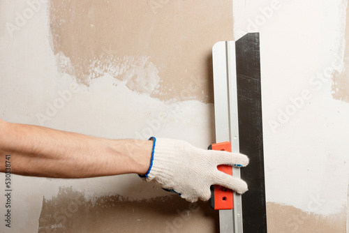 Professional plaster walls. Builder with plastering tools apartment wall repair. Master applies putty with a spatula to the reinforced joint of drywall close up. Home improvement concept. photo