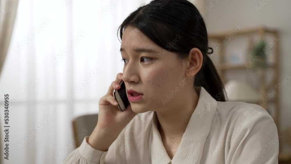 headshot of an asian woman entrepreneur talking on the smartphone with a serious look on face while working from home in the living room headshot of an asian woman entrepreneur talking on the smartphone with a serious look on face while working from home in the living room