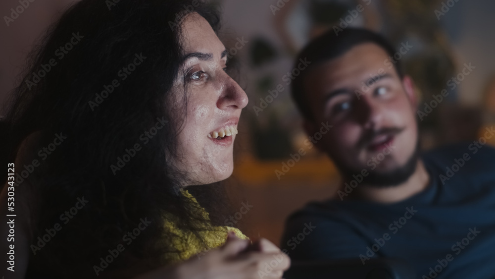 Woman with a disability and man rejoicing and discussing movie while watching it on TV together at home in the evening Woman with a disability and man rejoicing and discussing movie while watching it on TV together at home in the evening