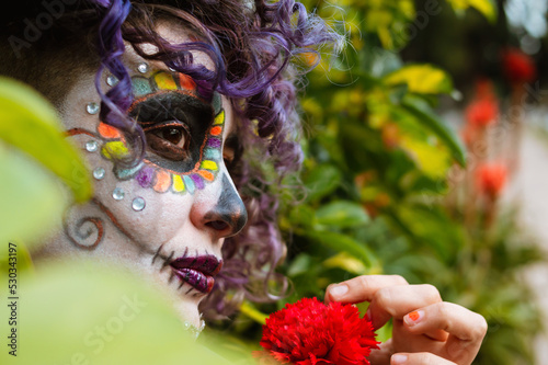 young latin woman with catrina makeup standing among the bushes in the cemetery.
