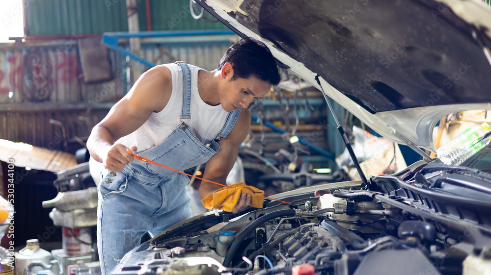 Young male mechanic worker in garage working repair service fix the car engine at old industry car garage workshop. Young male mechanic worker in garage working repair service fix the car engine at old industry car garage workshop.