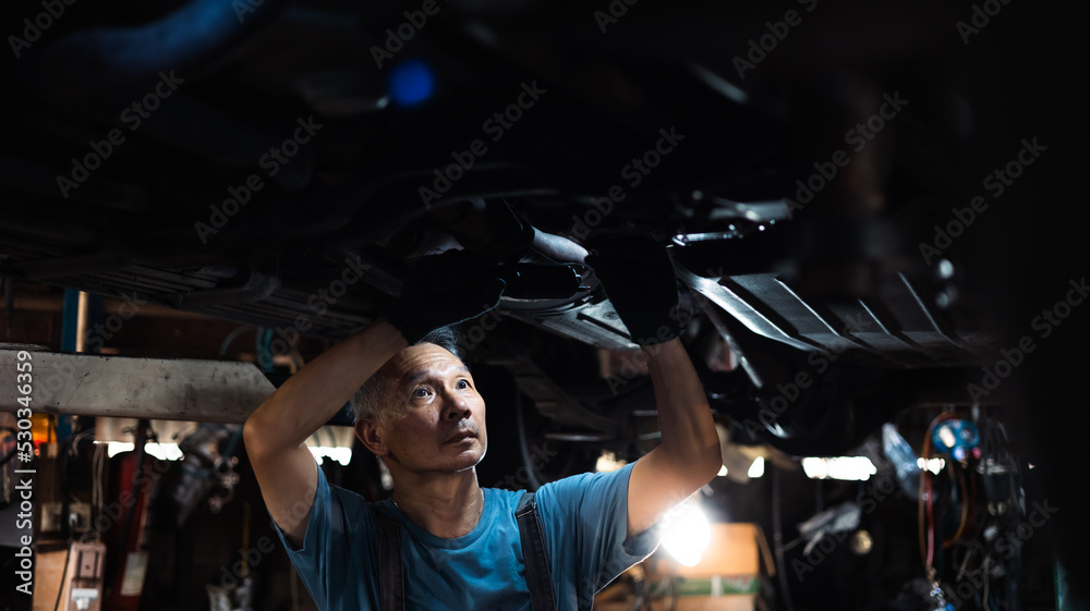 senior asian male mechanic engineering working under Vehicle in Car Service. Repair specialist, technical maintenance. Small business owner.