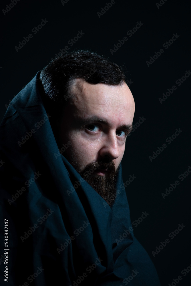 dramatic religious portrait of a bearded guy in a black cape on a dark background