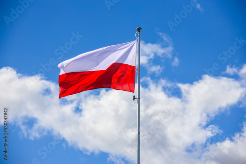Polska flaga biało-czerwona powiewająca na maszcie na tle błękitnego nieba photo