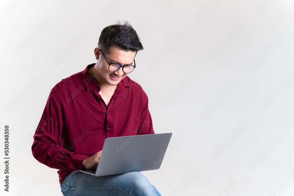 Asian man wearing a red shirt using laptop in studio grey background. The concept of freelance careers in the online world. Young Asian businessman.