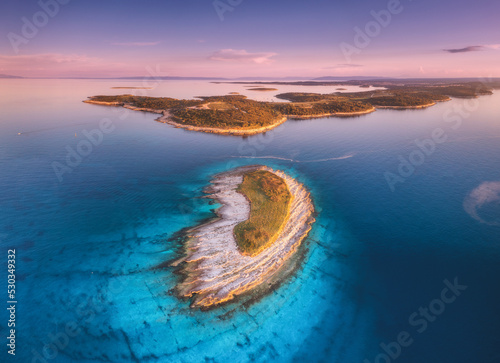 Aerial view of small island, Kamenjak cape, Adriatic sea, Croatia at sunset in autumn. Beautiful landscape with sea coast, mountains, clear water, purple sky at twilight in fall. Top view from drone
