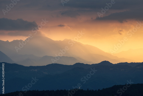 Amazing silhouettes of a mountains at colorful sunset in summer in Slovenia. Landscape with mountain ridges in fog, golden sunlight and clouds in the evening. Nature. Hills in sunlight. Scenery © den-belitsky