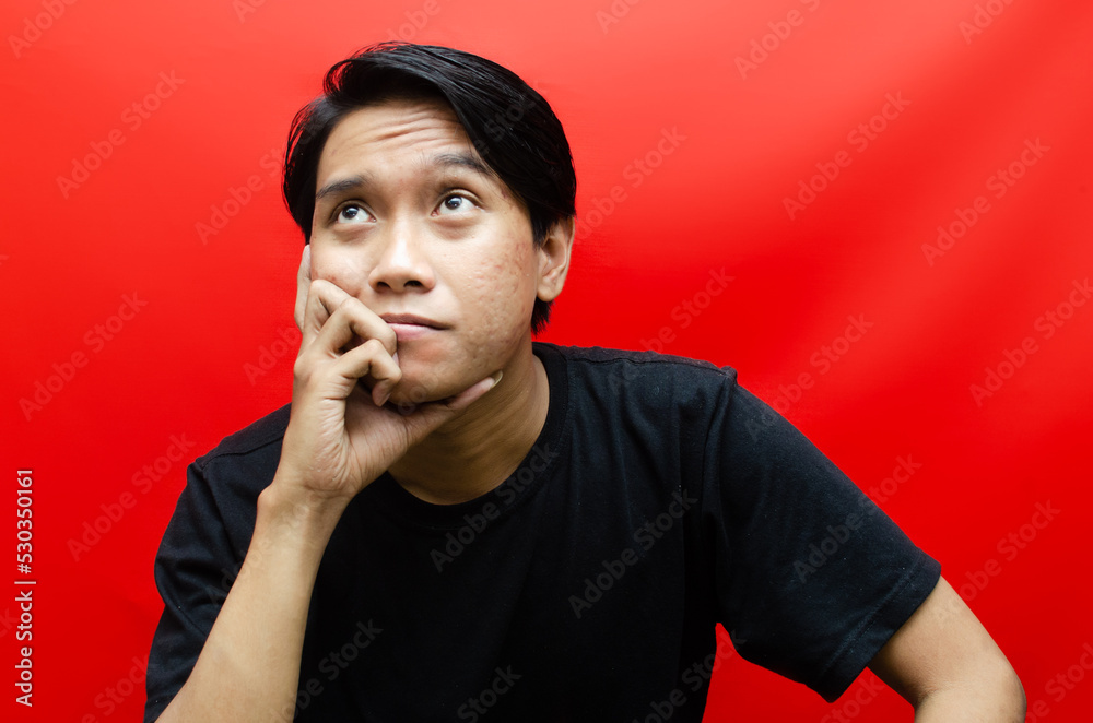 a young asian man in black t-shirt thinking and wondering with hand gesture isolated on red. a young asian man in black t-shirt thinking and wondering with hand gesture isolated on red.