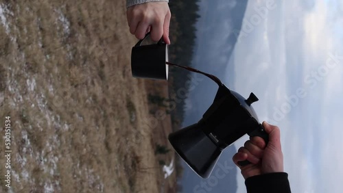 Person pouring out coffee from moka pot into cup outdoors with fog background photo