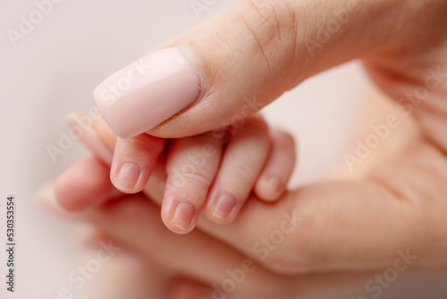 Close-up of a baby s small hand with tiny fingers and arm of mother on a white background. Newborn baby holding the finger of parents after birth The bond between mother and child Happy family concept