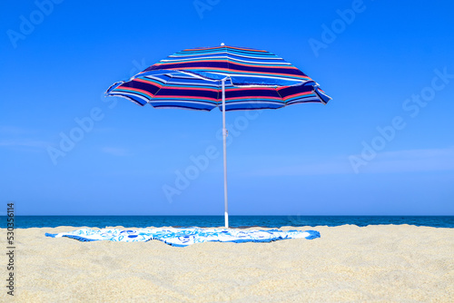 Beach umbrella, round towel on the sand. Shore sea