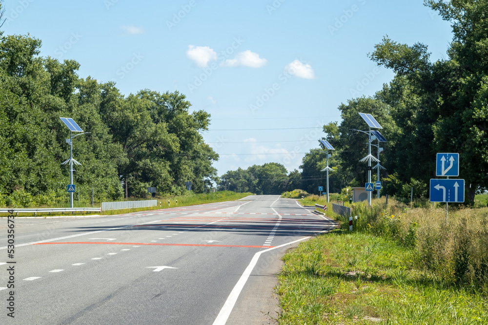 Lamp post with solar panel system on road with blue sky and trees. Autonomous street lighting using solar panels. Street lamp, on batteries from the sun. Alternative renewable energy systems.