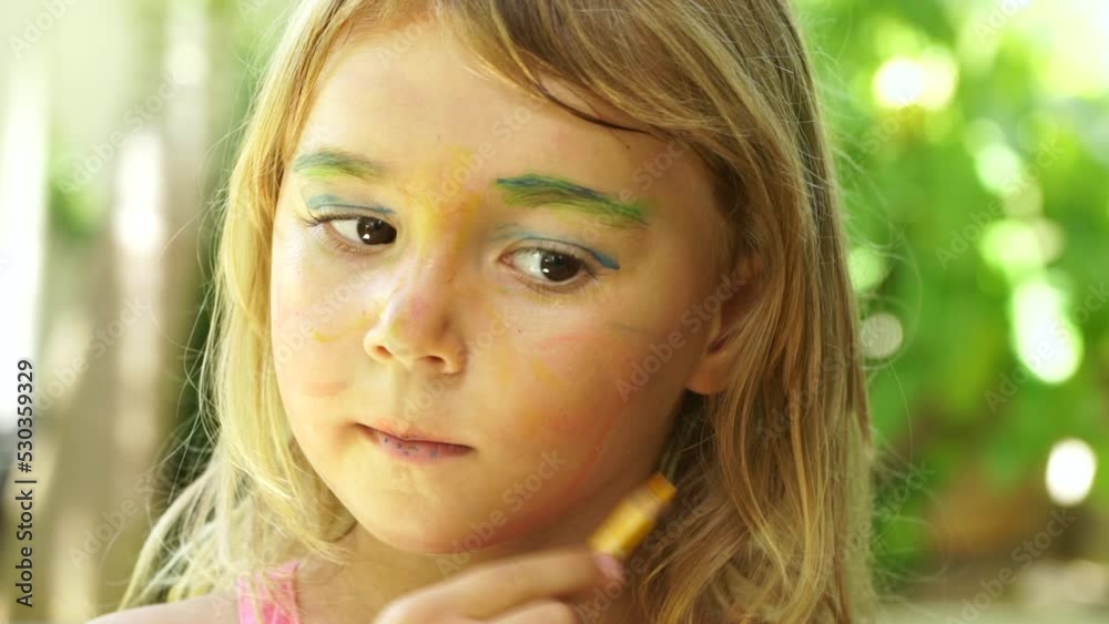 Close-up of little cute girl doing makeup with color pencils. She paints her face imitating mom or an adult woman Close-up of little cute girl doing makeup with color pencils. She paints her face imitating mom or an adult woman