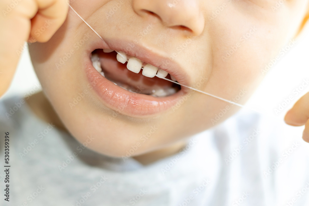 kid using dental floss to remove food rest from his milk teeth.child