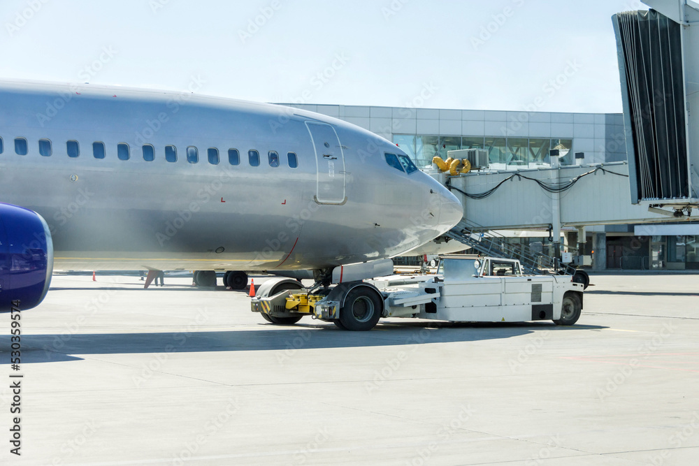 Commercial passenger airplane during push back operation. Shiny metal fuselage of the liner when departing from the air bridge gate. Commercial passenger airplane during push back operation. Shiny metal fuselage of the liner when departing from the air bridge gate.