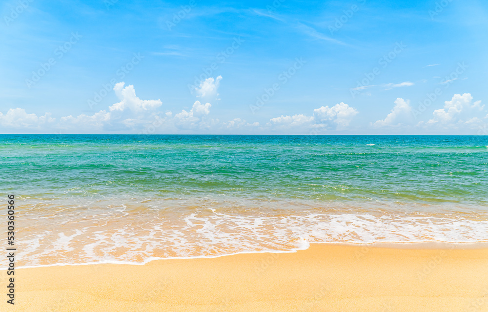 Landscape seaside view with sand beach white foamy wave from blue sea on daylight and blue sky white clouds background