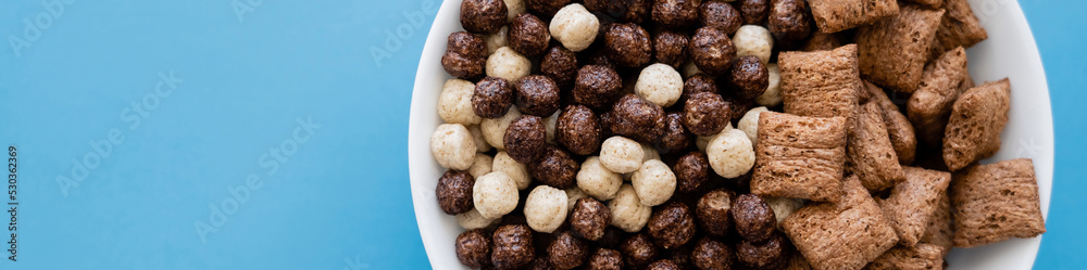 top view of bowl with tasty cereal balls and puffs isolated on blue, banner. top view of bowl with tasty cereal balls and puffs isolated on blue, banner.