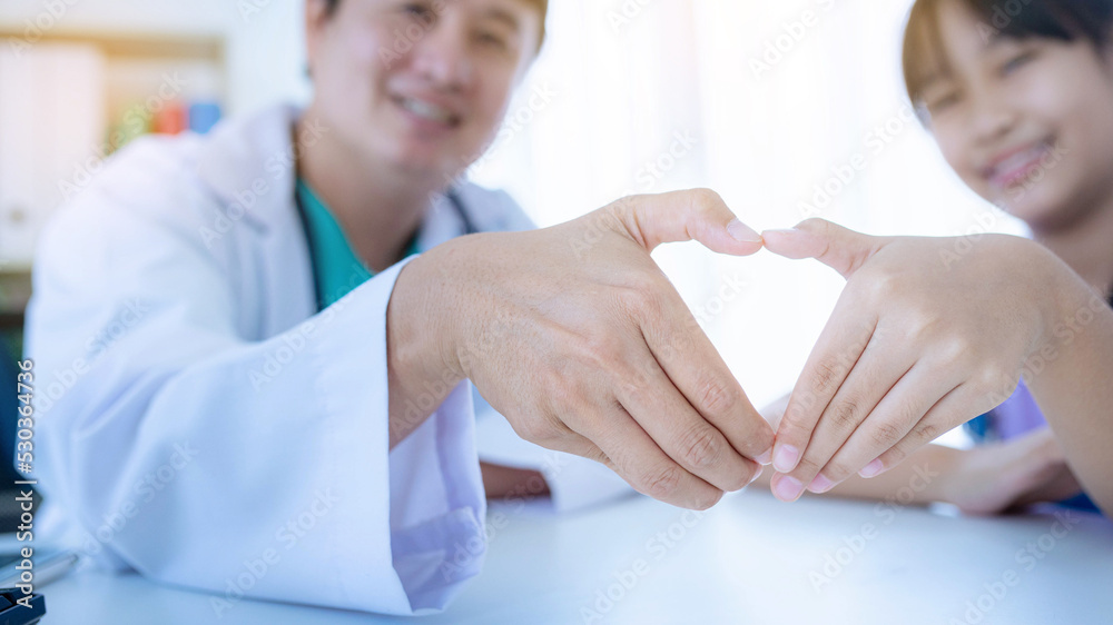 Young Asian girl and pediatrician forming a heart with their hands to celebrate her good health check results.