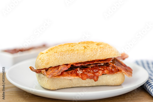 Closeup of crispy bacon in a sourdough roll on white plate