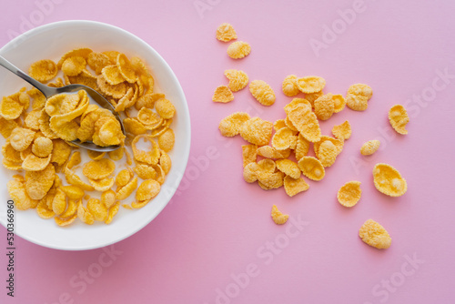 top view of bowl with corn flakes and organic milk on pink background.