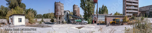 Panoramic photo of an old cement factory. An old dump truck and tractor made in the USSR.