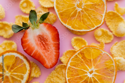 Fototapeta Naklejka Na Ścianę i Meble -  close up view of fresh sliced strawberry around crispy corn flakes and dried oranges on pink.