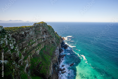 A spectacular view of towering stone cliffs at Cape Point, with the blue ocean and waves crashing below in the Table Mountain National Park.