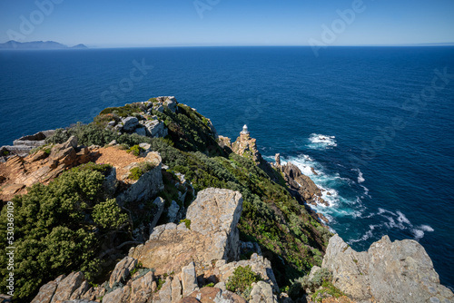 A spectacular view of the blue sea and the Cape Point lighthouse on top of Dias Point  with white surf breaking far below around Dias Rock.