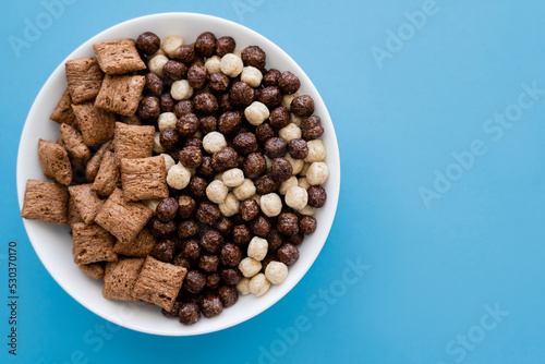top view of bowl with tasty cereal balls and puffs isolated on blue.