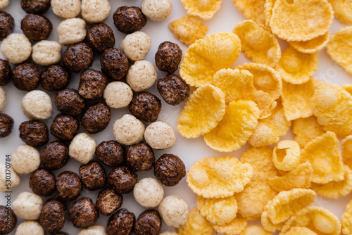close up of cereal balls with different flavors near corn flakes isolated on white.