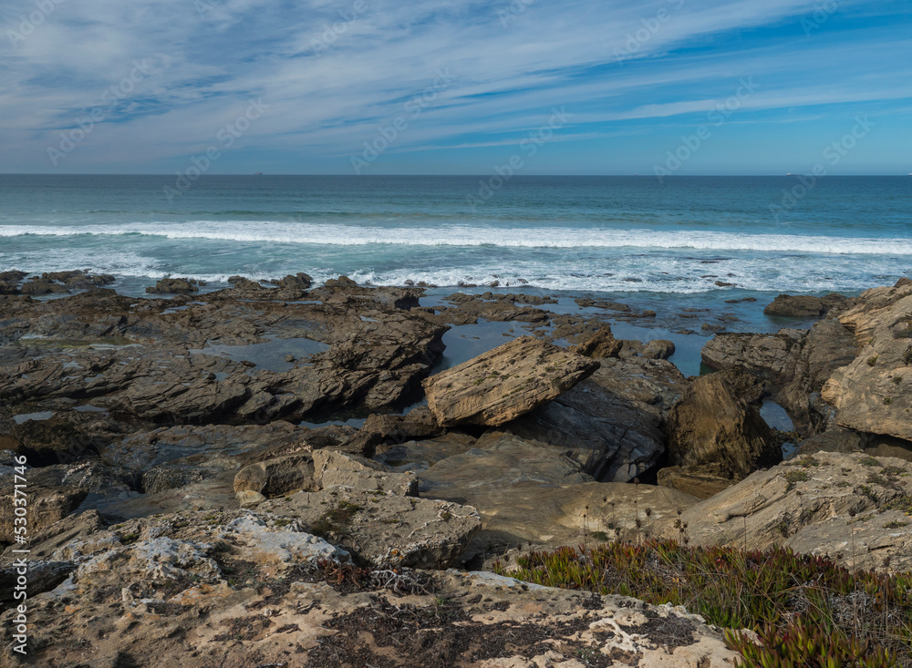 View sea shore with ocean waves, sharp rocks, stones and green vegetation at Rota Vicentina wild coast near Porto Covo, Portugal.