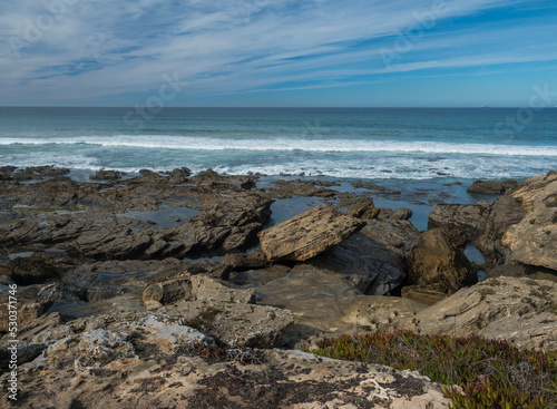 View sea shore with ocean waves, sharp rocks, stones and green vegetation at Rota Vicentina wild coast near Porto Covo, Portugal.