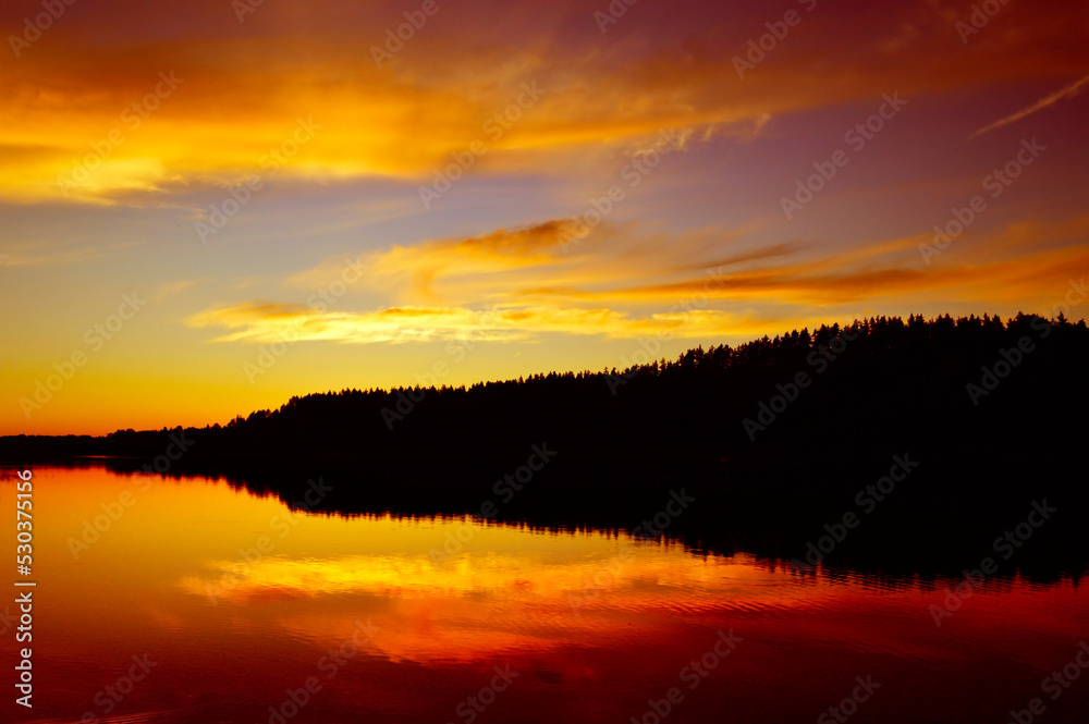 Wild nature, picturesque water landscape. Coniferous forest and red sunset sky are reflected in the water, ripples and waves on the water. Calm quiet evening, harmony. background, wallpaper, postcard