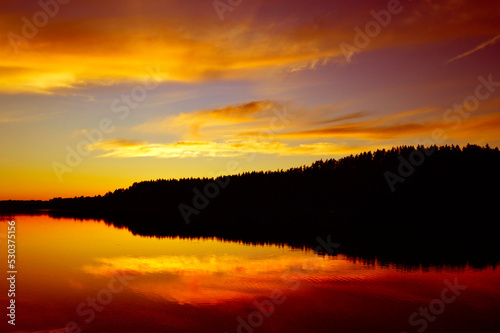 Wild nature, picturesque water landscape. Coniferous forest and red sunset sky are reflected in the water, ripples and waves on the water. Calm quiet evening, harmony. background, wallpaper, postcard