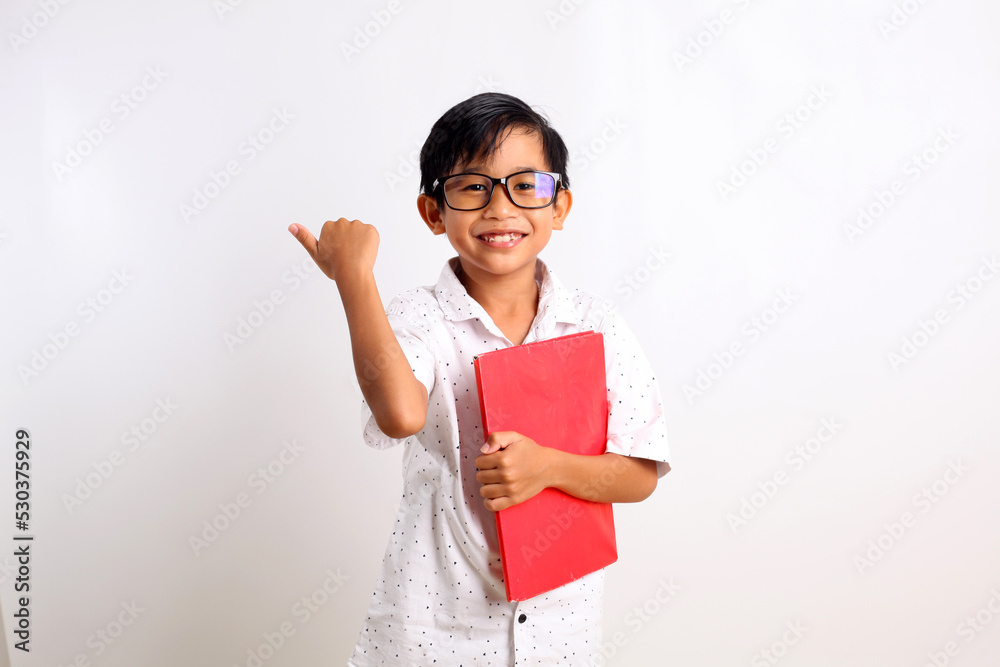 Adorable asian schoolboy carrying a book while presenting sideways. Isolated on white background Adorable asian schoolboy carrying a book while presenting sideways. Isolated on white background