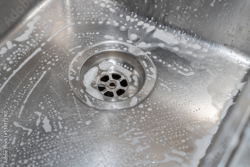 White foam with bubbles of cleane in a washbasin. Drain hole with soap bubbles in metal sink. photo