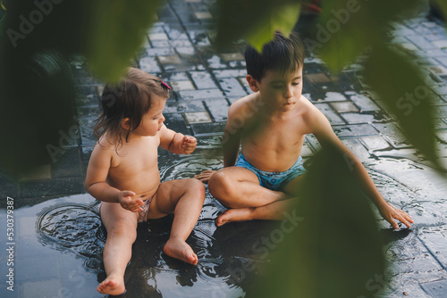 Two children standing in the garden naked, playing in the water that accumulated after the summer rain. Spring, summer garden. Summer outdoor fun activity photo