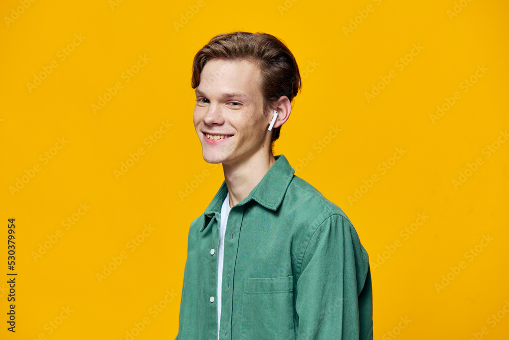 Fototapeta premium a guy in white wireless headphones stands against a yellow background in a green t-shirt. Horizontal photo with space for text