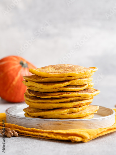 Pumpkin (squash) pancakes stack. Autumn breakfast, seasonal baing. Close up view. Orange crepes with honey and walnuts.