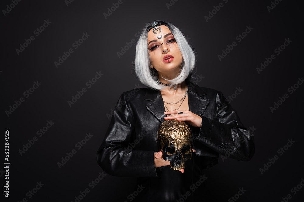 witch style woman with ash blonde hair holding golden skull isolated on black.