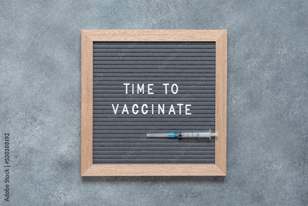 Time to vaccinate text on letter board with disposable syringe. Gray concrete grunge background. View from above, flat lay. Health concept.
