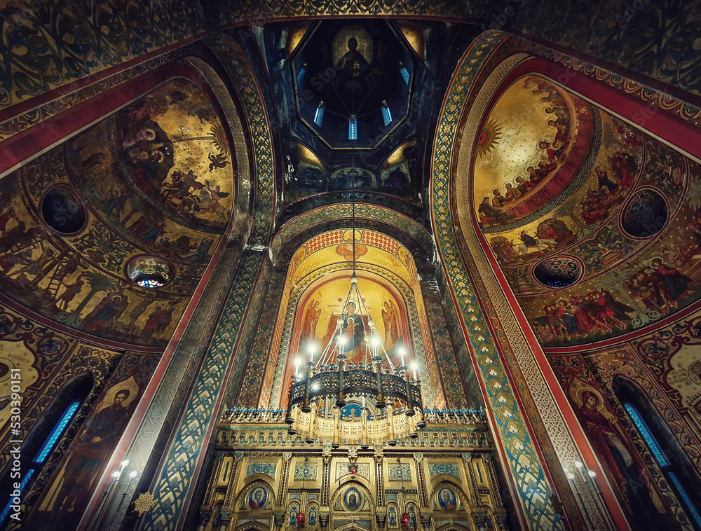 Interior architectural details of the Curtea de Arges monastery. The tall hall with painted icons, the golden altar and a chandelier with lights suspending out of ceiling