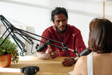 Young confident man voicing his point of view while recording interview with invited guest sitting in front of him during conversation